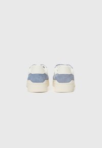 Sneakers with a suede material in light blue and white, featuring a low profile, rounded back, and textured beige rubber sole.