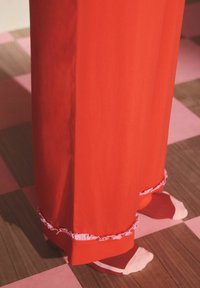 Punased püksid volangilise roosa äärega, mida on kombineeritud mitmevärviliste sokkidega. Taustal on mustriline põrand roosades ja puidutoonides.