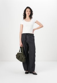 White short-sleeve fitted top, dark wide-leg pants, black flats, and a green fabric handbag with pockets, set against a white background.