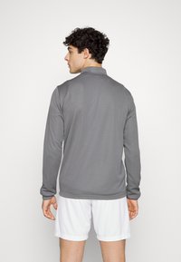 Grijze lange mouw polo met kraag, zachte textuur en een getailleerd ontwerp. Draag met witte shorts, gezien van achteren.