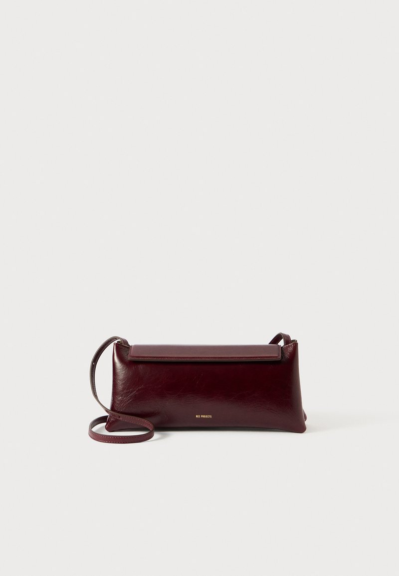 Burgundi bőr keresztbody táska sima textúrával, téglalap alakú, fedeles záródással és vékony, állítható pánttal. Arany logó részlet látható.
