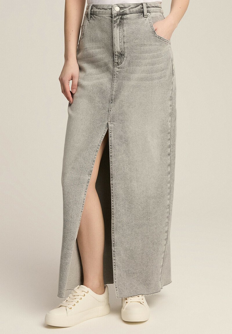 Szara dżinsowa spódnica maxi z rozcięciem z przodu, wysokim stanem i kieszeniami; zestawiona z białymi sneakersami dla casualowego looku.