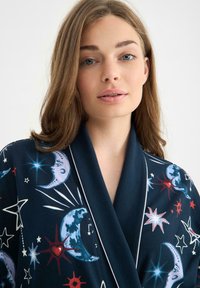 Marinblå kimono med himmelska tryck som föreställer månar och stjärnor i vitt, röd och blått. Slät tyg med sjalkrage och kantade detaljer.