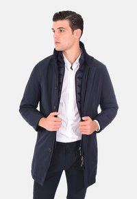Giacca outdoor blu navy con zip frontale, chiusura con bottoni, fodera interna trapuntata e colletto in piedi. Texture liscia e design moderno.