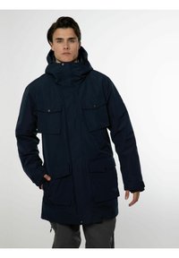 Parka bleu marine avec capuche, dotée de deux poches poitrine et de deux poches latérales, fabriquée en tissu lisse avec une finition légèrement mate.