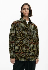 Vævet jakke med et lappe-design med houndstooth og striber i grønt, sort, orange og gult. Inkluderer to frontlommer.