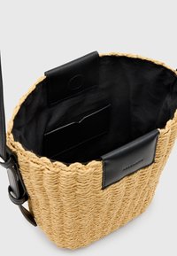 Borsa di paglia tonda intrecciata con parte superiore e tracolla in pelle nera, dotata di una tasca interna e di una fodera liscia.