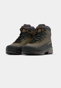 Kāpjotības zābaki ar tumši pelēku un olīvkrāsas dizainu, izturīgu materiālu, gumijas purngaliem, dzeltenām šņorēm un augstu potīšu atbalstu.