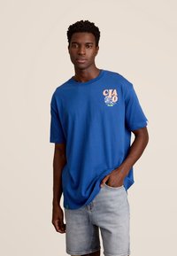 Blauwe katoenen t-shirt met "CIAO" grafiek in pastelkleuren, ontspannen pasvorm, ronde hals, korte mouwen, gecombineerd met lichte denimshorts.