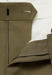 Tan fabric with a smooth texture features a zipper, tag loop, and white interior lining. Visible stitching along the edges and seams.
