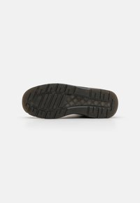 Suela de zapato de goma negra con surcos profundos, presentando una superficie lisa y texturizada y un borde ligeramente desgastado. Diseñada para ofrecer tracción y durabilidad.