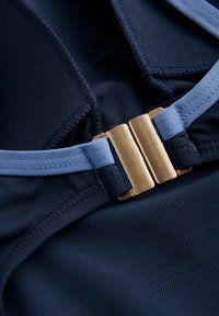 Marineblaues Gewebe mit einer glatten Textur verfügt über einen goldenen metallischen Verschluss und hellblaue Akzente. Die Nähte sind entlang der Kanten sichtbar.