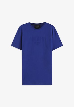 Camiseta azul de algodón con mangas cortas y cuello redondo. Presenta un texto sutil en relieve "FREDDY TRAINING DEPT." en el frente. Textura suave.