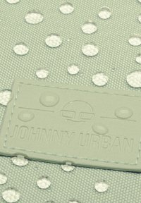 Svetlozelená tkanina s vyvýšenými bielymi bodkami a vodnými kvapkami. Obsahuje textúrovanú embosovanú koženú nálepku s nápisom "JOHNNY URBAN".