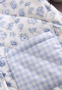 Tissu matelassé avec motif floral bleu et blanc sous un morceau plié de tissu vichy bleu et blanc.