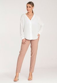 Biała bluzka z długim rękawem i dekoltem w serek, z guzikami, w połączeniu z jasnobeżowymi spodniami typu tapered. Przezroczyste sandały na blokowym obcasie dopełniają całość.