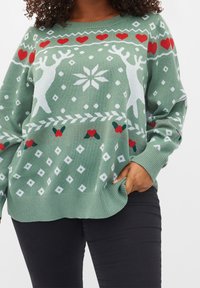 Hellgrüner Strickpullover mit Rentieren, Herzen und Schneeflockenmuster in Weiß und Rot. Lockere Passform mit gerippten Bündchen und Saum.