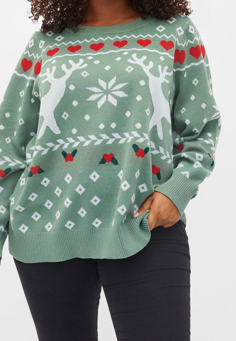 Hellgrüner Strickpullover mit Rentieren, Herzen und Schneeflockenmuster in Weiß und Rot. Lockere Passform mit gerippten Bündchen und Saum.