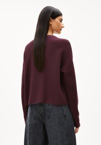 Burgunderfarbener Pullover mit lässiger Passform, gerippter Textur und weiten Ärmeln, kombiniert mit hochgeschnittenen, dunkelgrauen Jeans.