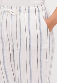 As calças em mistura de linho apresentam uma base branca com riscas verticais em azul claro e castanho. Cintura elástica com cordão e bolsos.