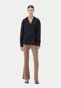 Svart omlottblus med knäppning, långa ärmar och v-ringning, kombinerad med bruna ribbade utsvängda byxor och svarta sandaler.