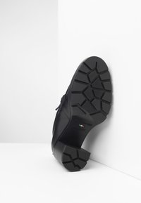 Scarpa in pelle nera con suola in gomma testurizzata, dotata di una presa con motivo. Marchio visibile sulla suola. Design elegante con accenti minimali.