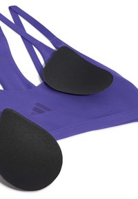 Brassière de sport violette avec coussinets noirs amovibles posés dessus sur fond blanc.