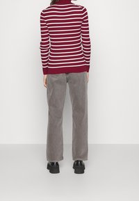 Pull rayé bordeaux et blanc avec col roulé, associé à un pantalon large gris et des chaussures noires épaisses ; tissus lisses et texturés.