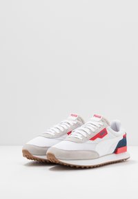 Bílé tenisky z materiálů síťoviny a semiše, s červenými a modrými akcenty, gumovou podrážkou a zavazováním na tkaničky. Na jazyku a boku mají logo.