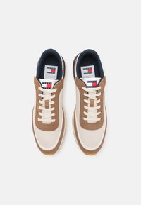 Zapatillas marrones y crema con cordones blancos, que cuentan con una parte superior texturizada, un forro azul marino y una lengüeta con marca que tiene un logo rojo y azul.