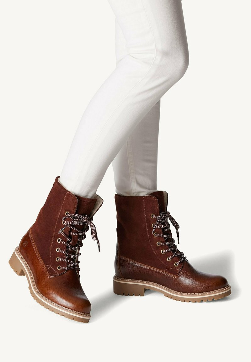 Bruine enkelboots van leer en suede. Voorzien van een ronde neus, gestructureerde accenten en decoratieve veters. De zool is voorzien van een patroon voor grip.
