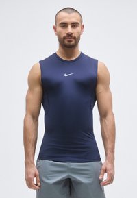 Top atletico senza maniche color blu navy con design aderente. Presenta un logo Nike bianco sul petto e cuciture a contrasto lungo i lati.