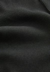 Gros plan sur un tissu noir côtelé avec des fines lignes verticales de tricot visibles et des plis subtils créant texture et profondeur.