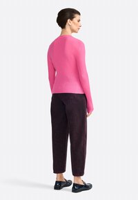 Pull en maille rose à manches longues, associé à un pantalon bourgogne foncé. Les chaussures présentent une finition noire brillante avec un design texturé.