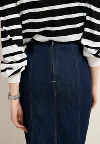 Gonna a matita in denim scuro con cerniera posteriore e cuciture visibili. Abbinata a una maglia a maniche lunghe a righe bianche e nere.