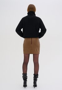 Maglione a collo alto nero lavorato a maglia, gonna mini in pelle marrone con zip sul retro, collant neri trasparenti e stivali neri con tacco morbidi.
