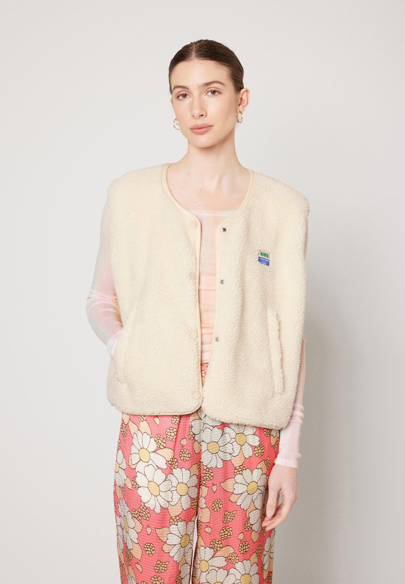 Crème-kleurige fleece vest met een ronde halslijn, drukknoopjes en zijzakken; heeft een klein blauw en groen logo patch.