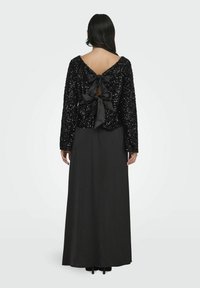 Haut noir à sequins avec des manches longues, doté d'un grand nœud en satin à l'arrière, associé à une longue jupe maxi noire.