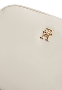 Τσάντα σε κρεμ απόχρωση με υφή και λεία επιφάνεια, με ανάγλυφο, χρυσό λογότυπο. Στρογγυλεμένες άκρες και μινιμαλιστικός σχεδιασμός.