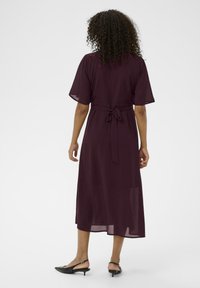 Paarse midi-jurk met korte, doorschijnende mouwen, een gestrikte taille en een vloeiende silhouet. Draag het met zwarte slingback-hakken, die een eenvoudig ontwerp tonen.