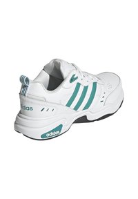 Vit idrottssko med teal tre ränder, texturerad läderövre, snörningsdesign och vadderad krage. Svart yttersula med logodetalj.