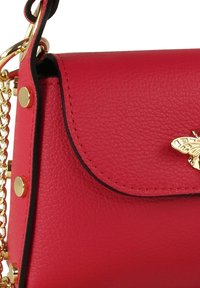 Rode leren handtas met een gestructureerde afwerking, voorzien van een gouden bijaccent en een kettingriem. De sluiting is een klep met afgeronde randen en gouden beslag.