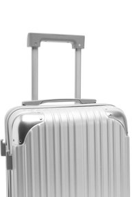 Srebrna walizka z twardą skorupą z pionowymi żłobieniami, metalowymi narożnikami oraz wysuwanym uchwytem. Materiał wydaje się solidny i trwały.