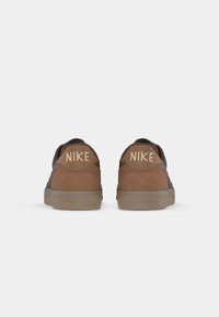 Pair of brown Nike sneakers shown from the back with beige Nike logo on heel tabs and gray rubber soles on a white background.