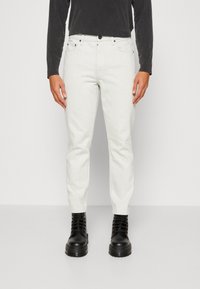 Pantaloni in denim bianco con vestibilità slim, dotati di chiusura con bottone frontale, due tasche laterali e stivali neri a contrasto.