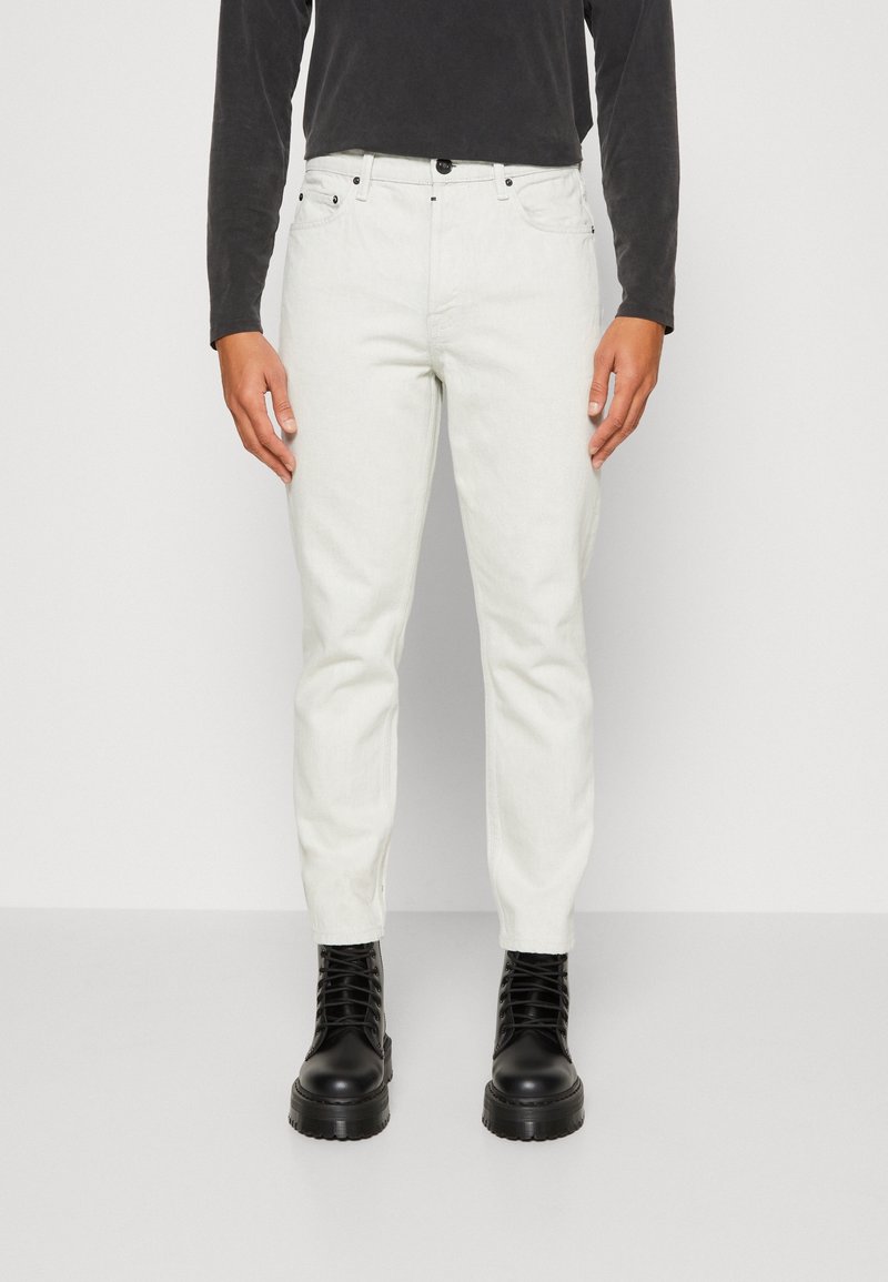 Pantaloni in denim bianco con vestibilità slim, dotati di chiusura con bottone frontale, due tasche laterali e stivali neri a contrasto.