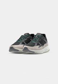 Gray and black sneakers with green laces; made of mesh and suede, featuring a curved white rubber sole and panels for added texture.