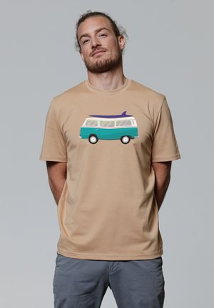 Beige t-shirt met een grafisch ontwerp van een teal en witte retro bus met een surfplank op het dak. Zachte katoen, korte mouwen, relaxte pasvorm.