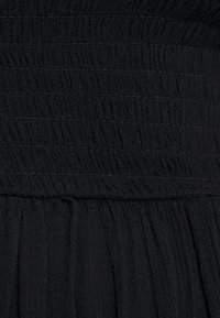 Černá tkanina s texturovanými smockingovými detaily nahoře a splývavými záhyby níže, vyrobená z jemného, lehkého materiálu s decentním leskem.