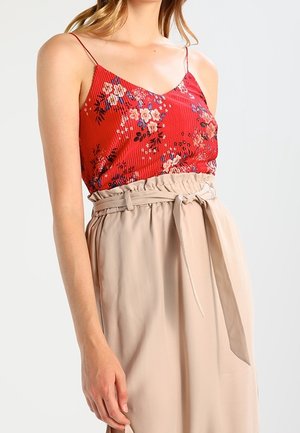 Top senza maniche con stampa floreale rossa e scollo a V, abbinato a una gonna beige a vita alta con vita arricciata e tessuto fluido.